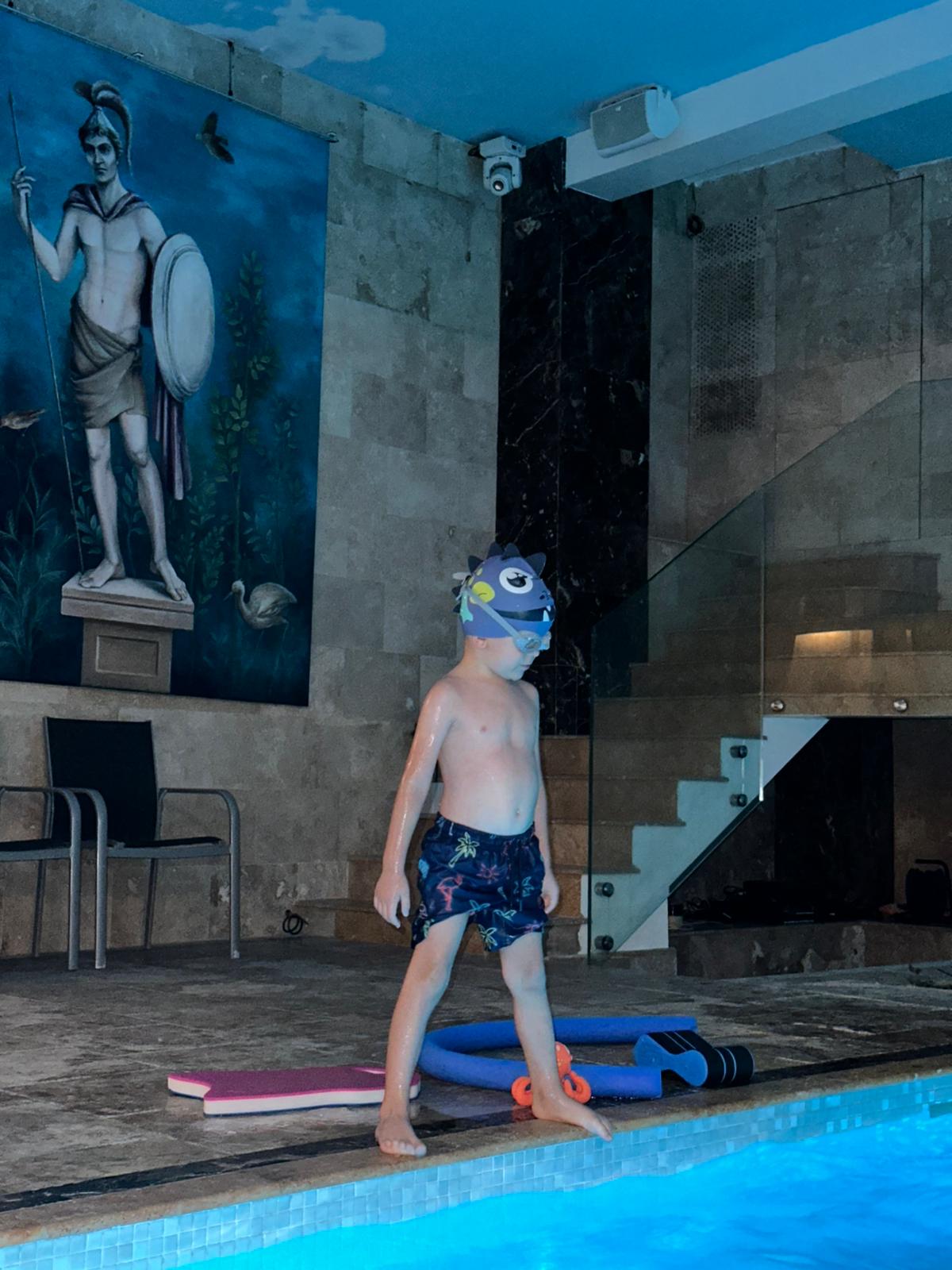 baietel-imbracat-in-echipament-de-inot-care-sta-pe-marginea-piscinei